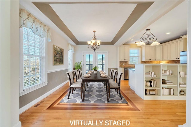 dining space featuring light wood-style flooring, visible vents, baseboards, a raised ceiling, and an inviting chandelier