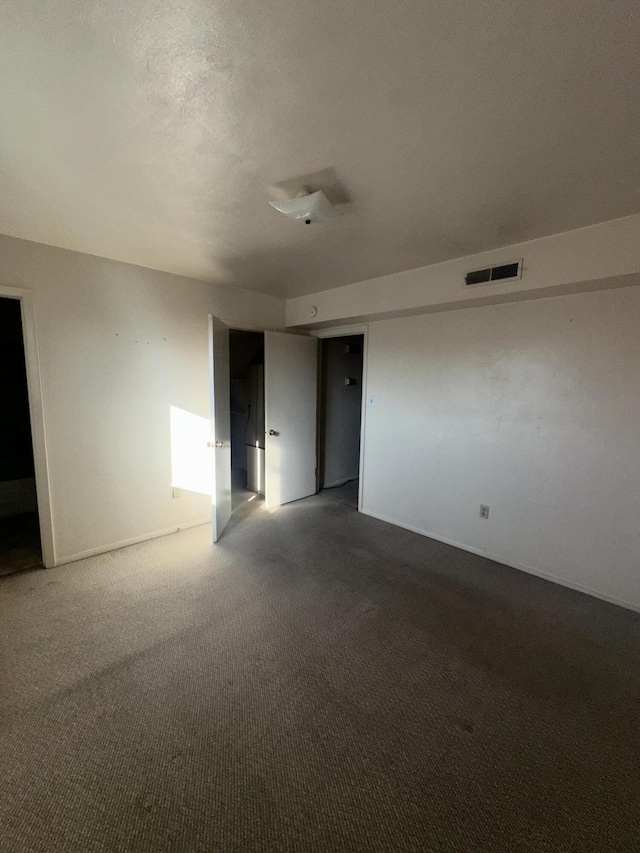 unfurnished room featuring dark colored carpet, visible vents, and a textured ceiling