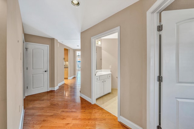 corridor with light wood-style floors, baseboards, and a sink