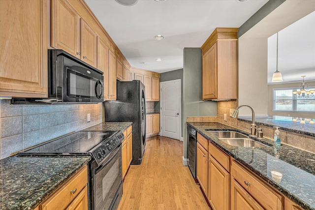 kitchen featuring decorative light fixtures, light wood-style floors, a sink, dark stone counters, and black appliances