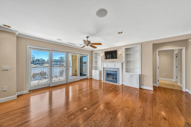 unfurnished living room featuring baseboards, crown molding, a tiled fireplace, and light wood-style floors