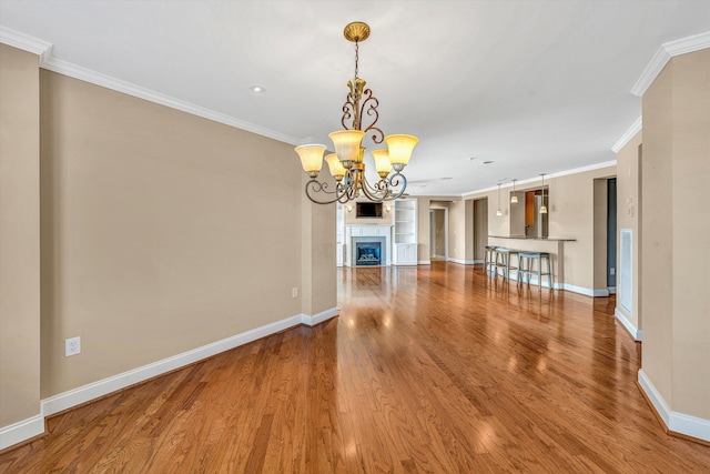 unfurnished living room featuring baseboards, ornamental molding, wood finished floors, an inviting chandelier, and a fireplace