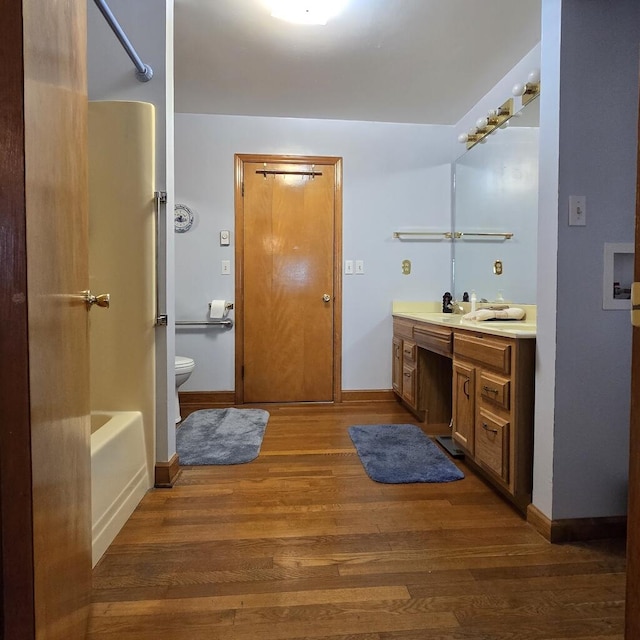 bathroom with toilet, wood finished floors, vanity, baseboards, and  shower combination