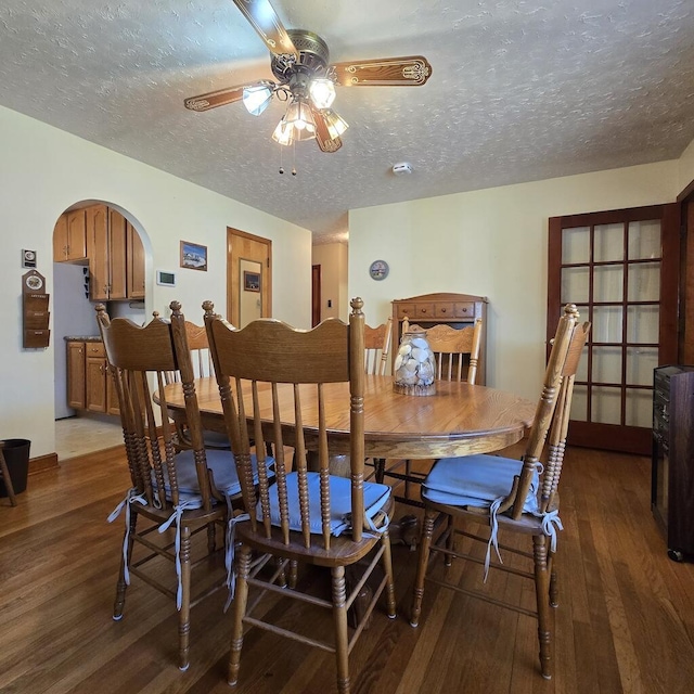 dining space with dark wood-type flooring, arched walkways, a textured ceiling, and a ceiling fan