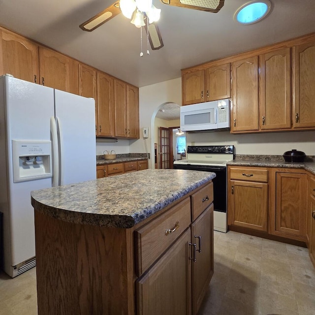 kitchen featuring white appliances, arched walkways, a ceiling fan, a kitchen island, and brown cabinets