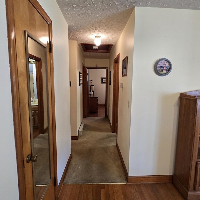 corridor featuring attic access, baseboards, a textured ceiling, and wood finished floors