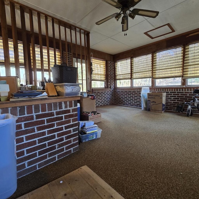 misc room with a ceiling fan, carpet, and brick wall