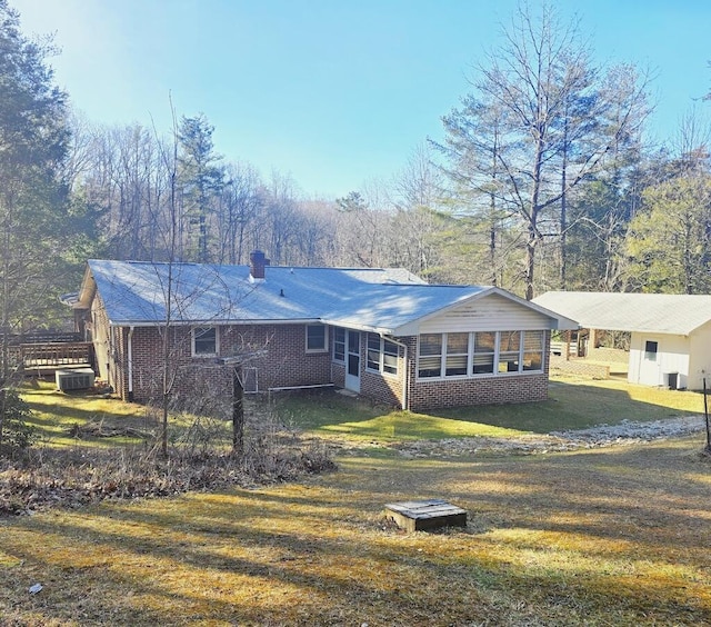 rear view of house featuring a sunroom, a chimney, an attached carport, a yard, and brick siding