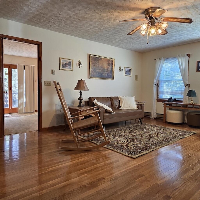 living area featuring a ceiling fan, a textured ceiling, baseboards, and wood finished floors