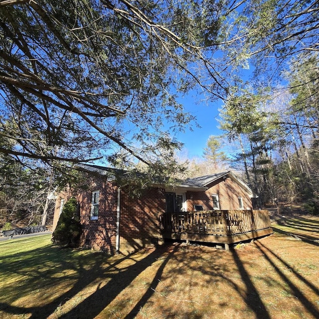 view of property exterior featuring a deck, brick siding, and a lawn