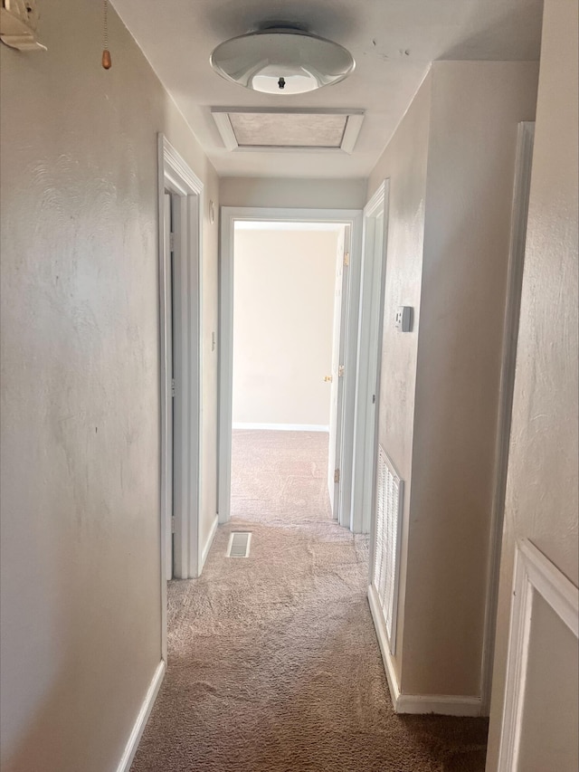 corridor with carpet floors, attic access, visible vents, and baseboards