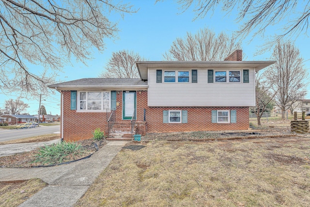 tri-level home featuring brick siding, a chimney, and fence