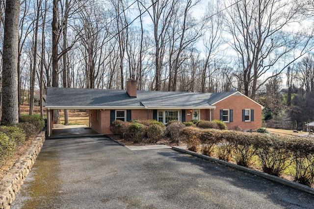 ranch-style home with a chimney, aphalt driveway, a carport, and brick siding