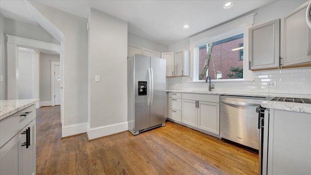 kitchen featuring appliances with stainless steel finishes, a sink, light stone countertops, light wood-style floors, and backsplash