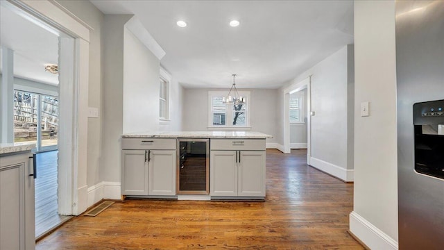 kitchen featuring light stone counters, decorative light fixtures, wood finished floors, beverage cooler, and a peninsula