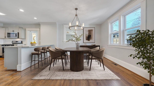 dining space with a notable chandelier, wood finished floors, visible vents, and baseboards