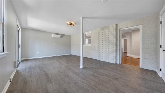 empty room featuring dark wood-style floors, brick wall, baseboards, and a wall mounted air conditioner