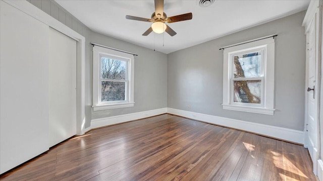 empty room featuring dark wood-style flooring, visible vents, ceiling fan, and baseboards