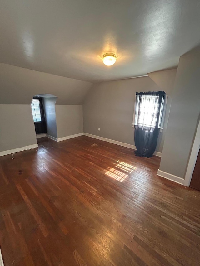 additional living space featuring lofted ceiling, dark wood-type flooring, plenty of natural light, and baseboards