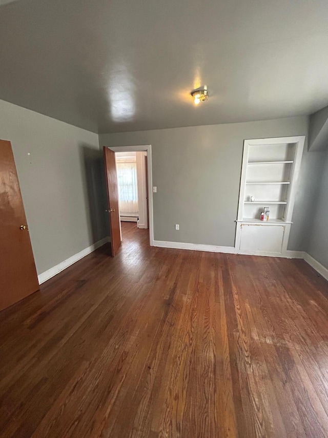 unfurnished living room featuring dark wood-style floors, built in shelves, and baseboards