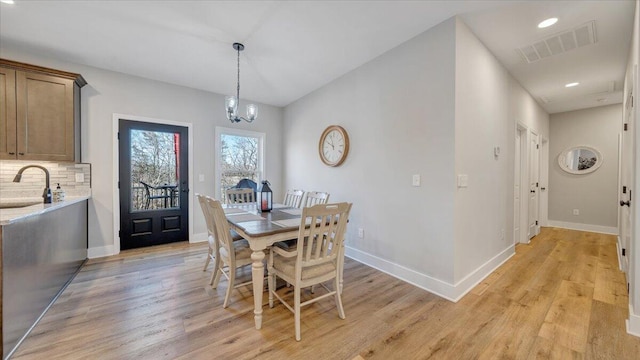 dining space featuring a notable chandelier, light wood-style flooring, visible vents, and baseboards