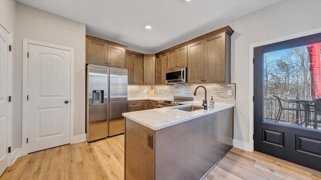 kitchen featuring light stone counters, light wood finished floors, backsplash, appliances with stainless steel finishes, and a sink