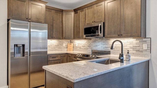 kitchen featuring appliances with stainless steel finishes, a sink, a peninsula, and light stone counters