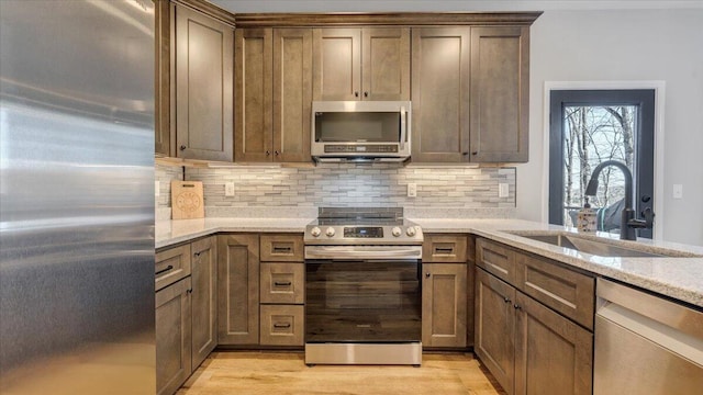 kitchen with a sink, appliances with stainless steel finishes, decorative backsplash, light stone countertops, and light wood finished floors