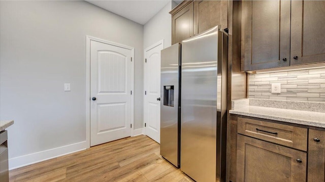 kitchen with baseboards, light wood-type flooring, backsplash, and stainless steel fridge with ice dispenser