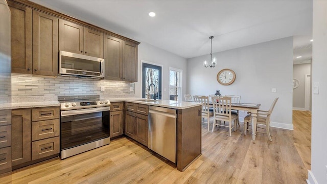 kitchen with pendant lighting, backsplash, appliances with stainless steel finishes, a sink, and a peninsula