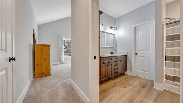 bathroom featuring vaulted ceiling, wood finished floors, vanity, and baseboards