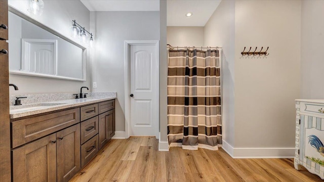 bathroom featuring double vanity, wood finished floors, a sink, and baseboards