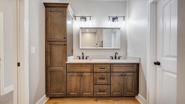 bathroom with wood finished floors, a sink, baseboards, and double vanity