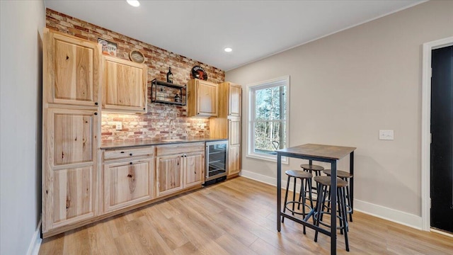 kitchen with dark countertops, wine cooler, light wood-type flooring, light brown cabinets, and a sink