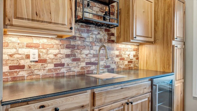 kitchen featuring wine cooler, light brown cabinets, brick wall, a sink, and dark countertops