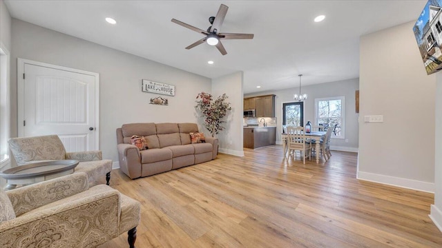 living room featuring ceiling fan with notable chandelier, light wood-type flooring, baseboards, and recessed lighting