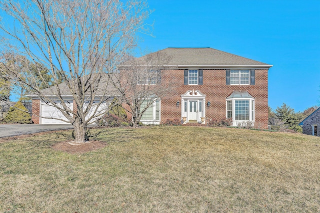 colonial house featuring aphalt driveway, an attached garage, brick siding, roof with shingles, and a front lawn