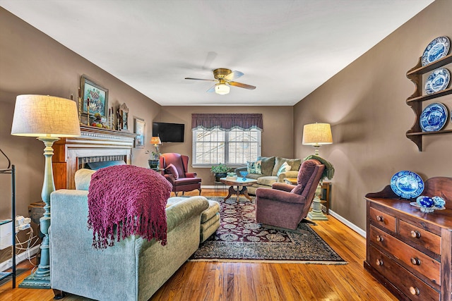 living room featuring a brick fireplace, ceiling fan, baseboards, and wood finished floors