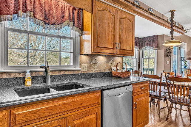 kitchen featuring a sink, backsplash, dishwasher, brown cabinetry, and dark countertops