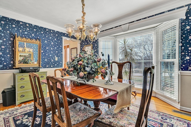 dining room with ornamental molding, wood finished floors, a notable chandelier, and wallpapered walls