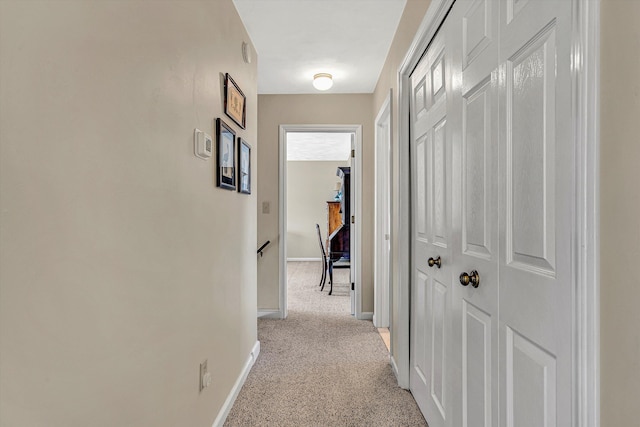 corridor with an upstairs landing, baseboards, and light colored carpet