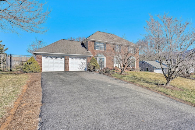 colonial-style house with a garage, driveway, brick siding, fence, and a front yard