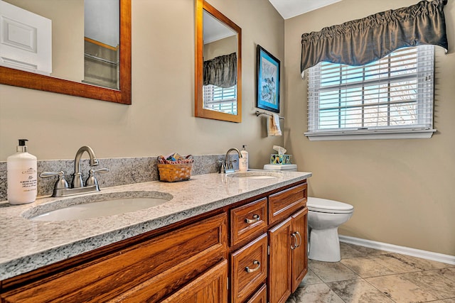 bathroom with double vanity, a sink, toilet, and baseboards