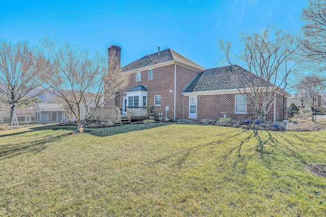 rear view of property featuring brick siding, a lawn, a chimney, and a wooden deck