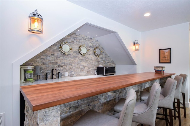 bar with a bar, stainless steel microwave, vaulted ceiling, and recessed lighting