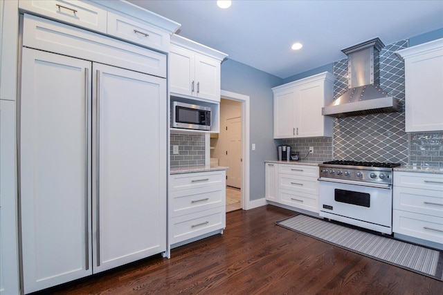 kitchen with light stone countertops, white cabinetry, wall chimney range hood, and built in appliances