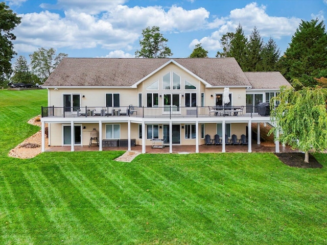 rear view of property with a deck, a patio, a lawn, and roof with shingles