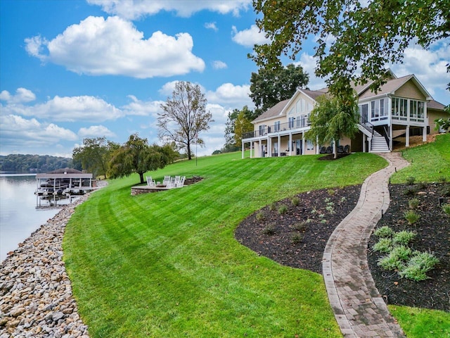 view of yard with a water view, stairway, an outdoor fire pit, a sunroom, and a boat dock