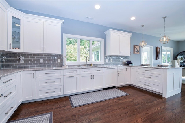 kitchen featuring dishwashing machine, a sink, visible vents, white cabinets, and hanging light fixtures