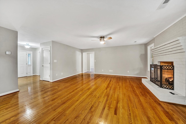 unfurnished living room with baseboards, visible vents, a ceiling fan, light wood-type flooring, and a brick fireplace